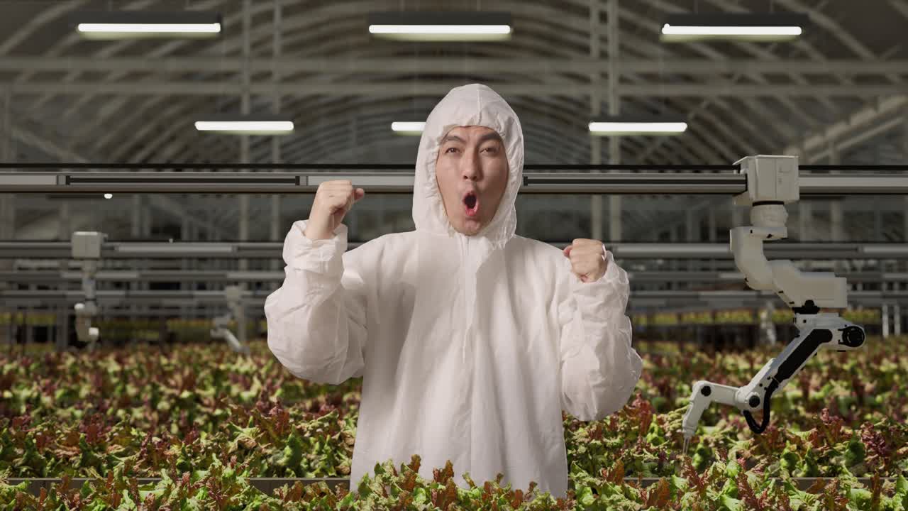 아시아 남성 연구원은 똑똑한 로 농부들과 함께 온실에 서서 축하하는 목표를 외치고 있습니다.