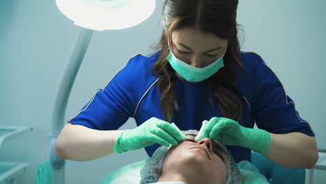 beautician in green gloves squishes pimples on client face