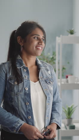 pensive indian woman in denim jacket looks out bright window dreaming about future. young housewife with ponytail smiles feeling happy in morning