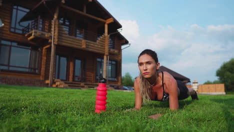 beautiful-brunette-on-the-background-of-a-large-mansion-engaged-in-fitness-and-performs-plank-exercise-for-the-press,-training-outdoors