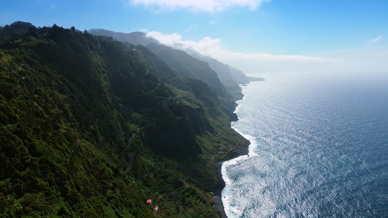 Amazing green slopes of the huge mountains at the Madeira Islands, Portugal. Touristic wavy paths go down to the waterscape of the ocean. Aerial view.