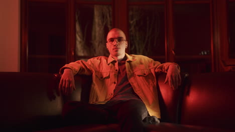 man in a yellow jacket on a couch in a red lit room