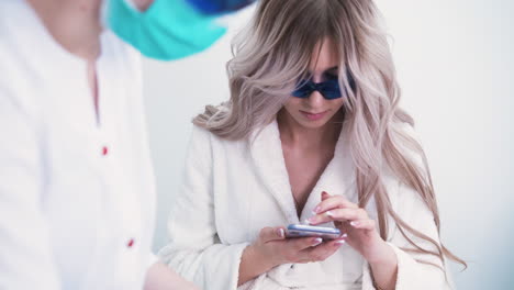 una mujer con un teléfono inteligente se somete a una depilación láser en un salón