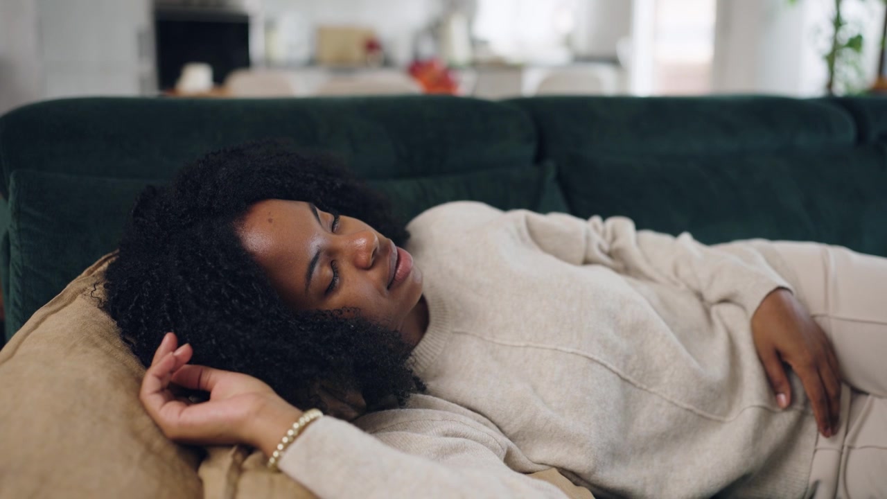 Fredfyldt afroamerikansk kvinde sover på sofaen derhjemme