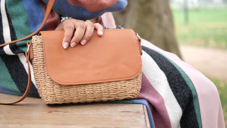 frau sitzt auf einer bank mit einer braunen gewebten tasche