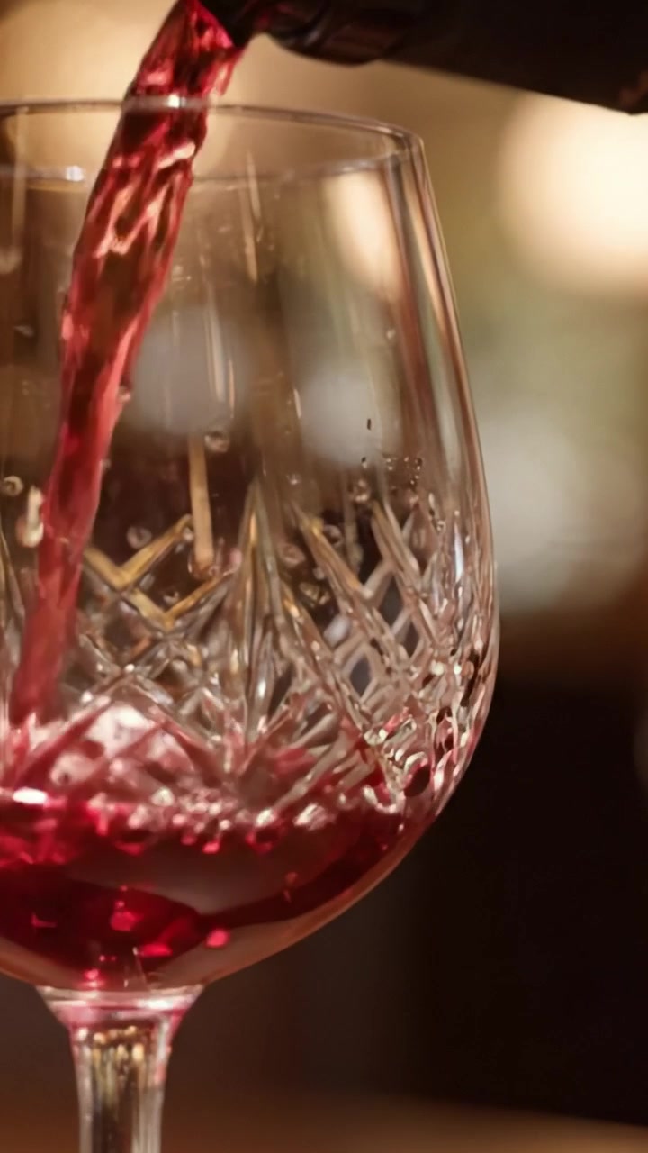 Un primo piano accattivante di un elegante calice di cristallo riempito con ricco vino rosso, che mostra dettagli intricati e riflessi in un ambiente caldo.