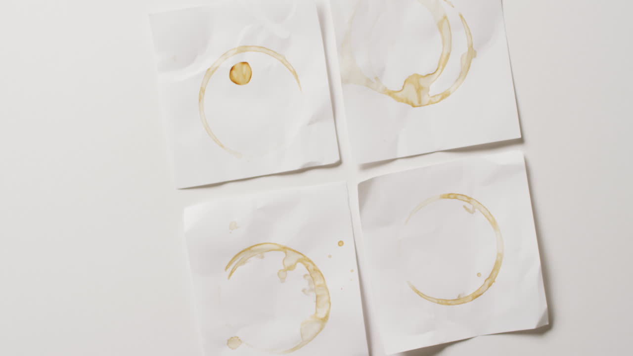 vídeo de primer plano de cuatro piezas de papel con manchas de taza de café sobre un fondo blanco