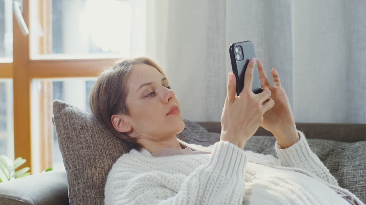 스마트폰을 사용하여 소파에서 휴식을 취하는 여성