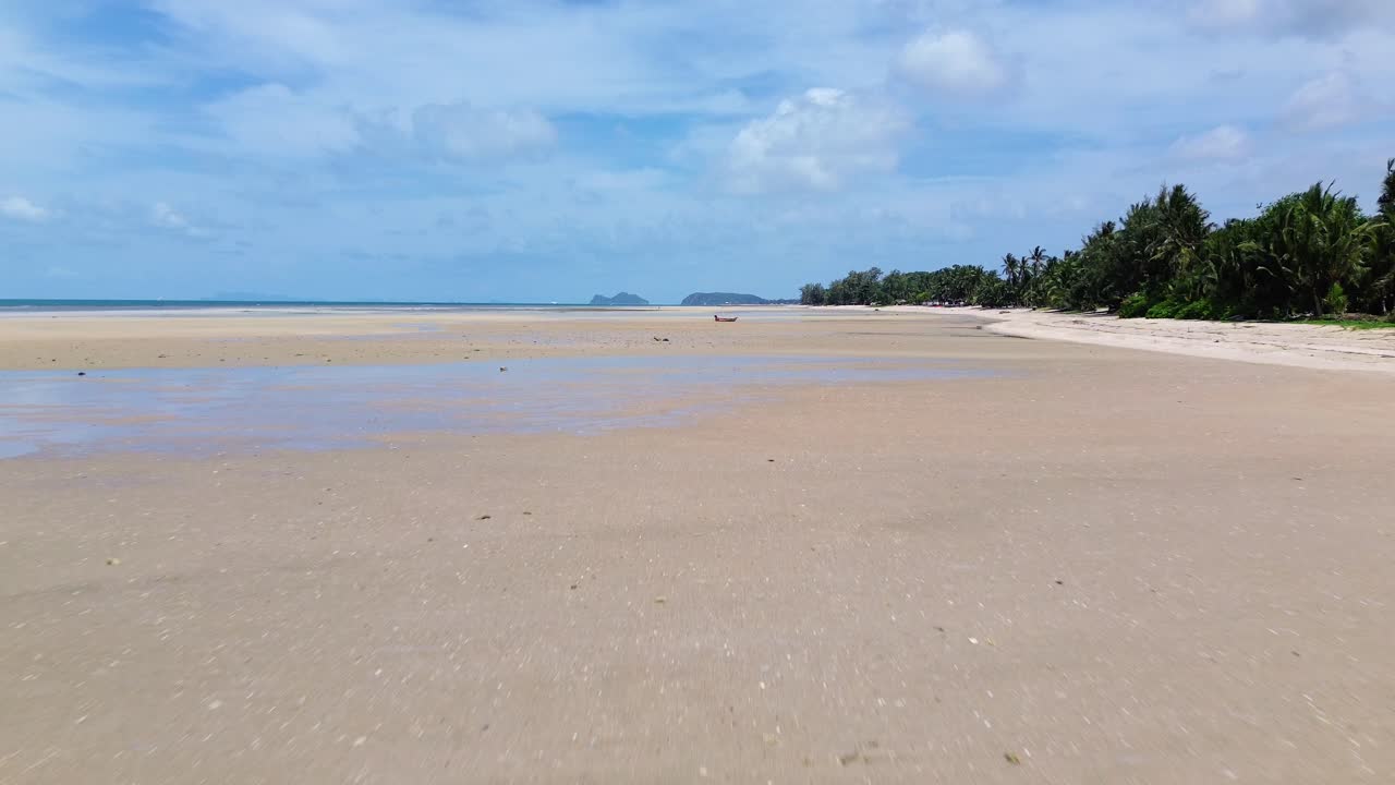 Drone video shows traditional small fishing boats anchored near the sandy shoreline of Koh Phangan, Thailand, with clear turquoise water and lush green coastline creating a scenic tropical seascape