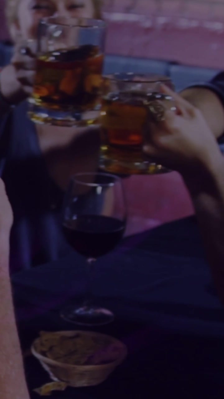 Video verticale: Un uomo che tiene una tazza, un braccio che si allunga, amici che brindano con boccali di birra in un bar.
