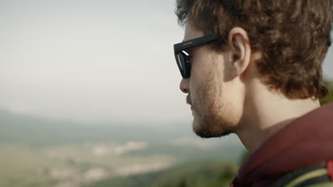 Hiker-holding-a-paper-map-looking-at-it-and-tha-into-the-distance-to-orient-himself,-wearing-dark-sunglasses