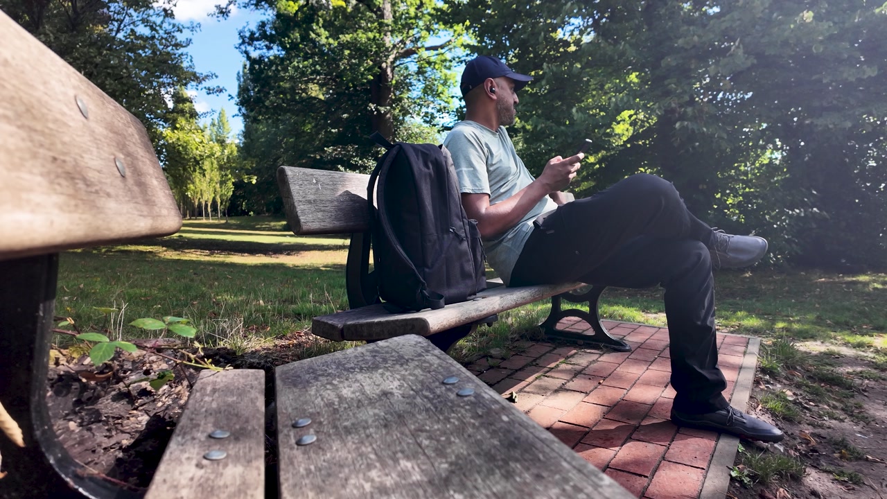 South asian freelancer working remotely using smartphone, taking a break in a park