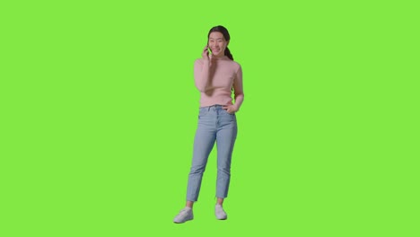 Full-Length-Studio-Shot-Of-Smiling-Woman-Answering-Mobile-Phone-Against-Green-Screen