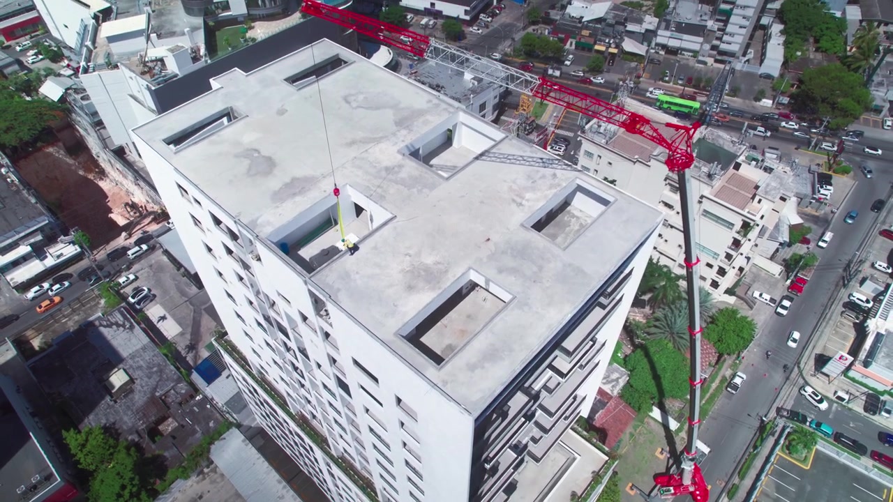 Toma aérea de dron en picada, alejándose y elevándose desde una vista cenital de una grúa torre roja en la azotea de un rascacielos en construcción en Santo Domingo
