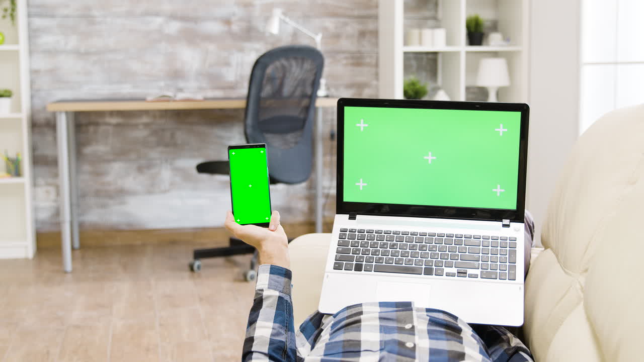 Man using laptop and smartphone with green screen