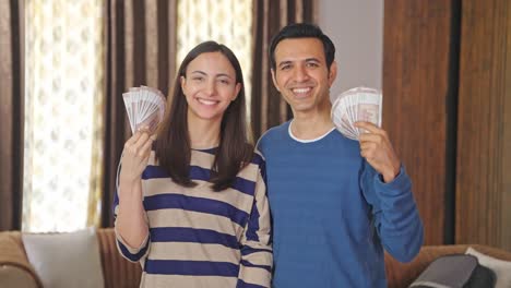 successful indian couple using money as fan