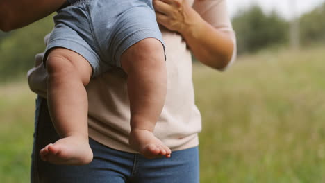 close up of an unrecognizable baby boy moving his naked legs while his mother holding him in the park