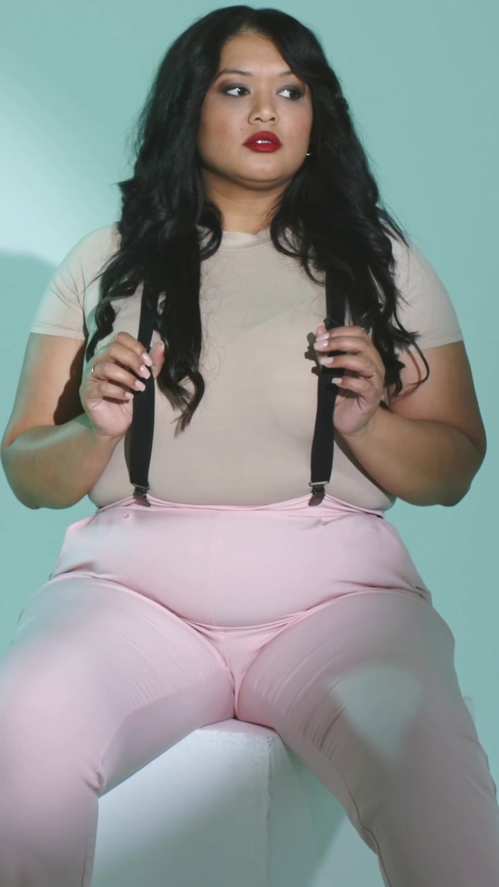 Video verticale: Telecamera in funzione, donna che sistema le bretelle nere sui pantaloni rosa per un servizio fotografico in studio.