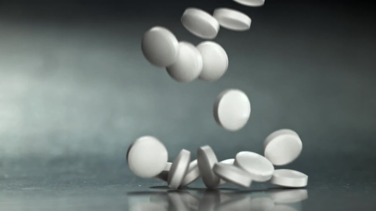 Pastillas blancas cayendo y dispersándose sobre una superficie reflectante en cámara lenta