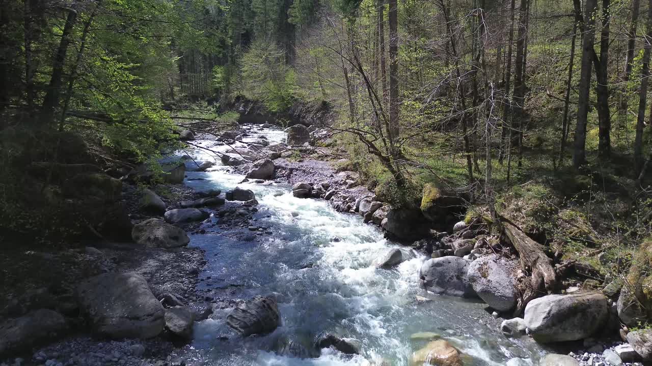 Drone bevæger sig langsomt op ad bjergflod omgivet af idyllisk skov