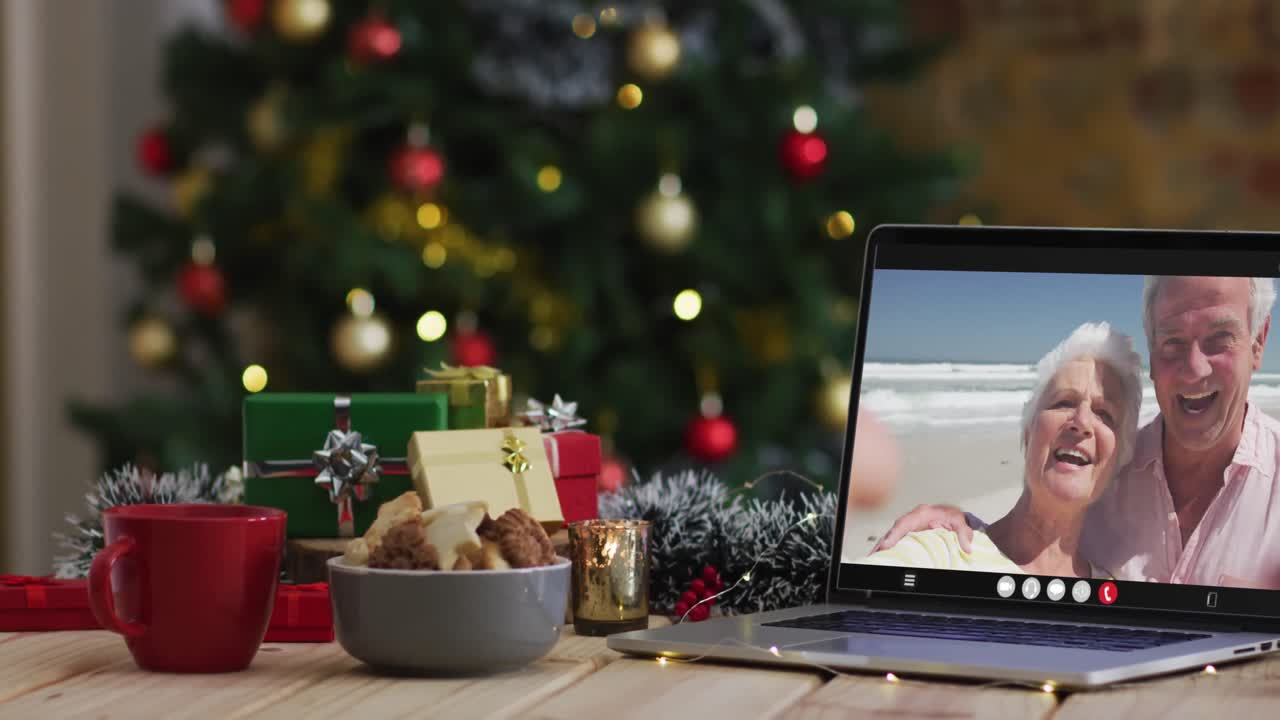 una pareja de alto nivel caucásica saludando en una videollamada en una computadora portátil, con un árbol de navidad
