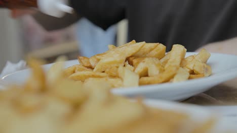 Hand-Pouring-Salt-and-Vinegar-on-British-Chips-Before-Eating-Close-Up-Lunchtime