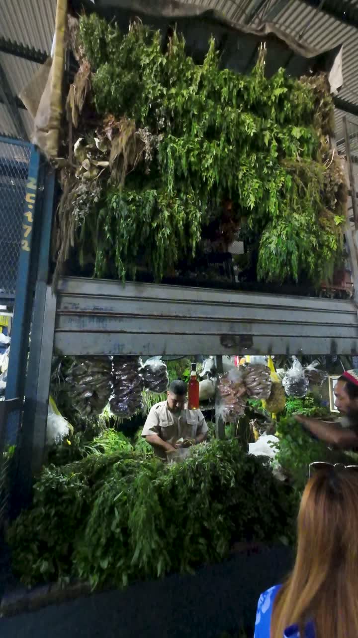 Market stall piled high with various fresh green herbs and plants, with male vendors below. Botany concept