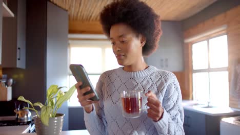 mujer afroamericana feliz usando un teléfono inteligente en una cabaña de madera