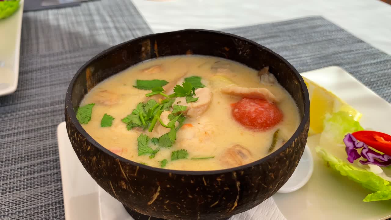 sopa de coco tailandesa picante con pollo y verduras en un tazón de coco, plato caliente en el restaurante de cocina tailandesa, toma de 4k