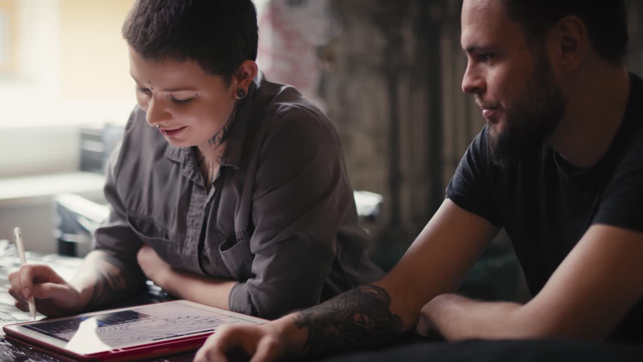 primer plano de un artista del tatuaje caucásico diseñando motivos en una tableta digital para un cliente.