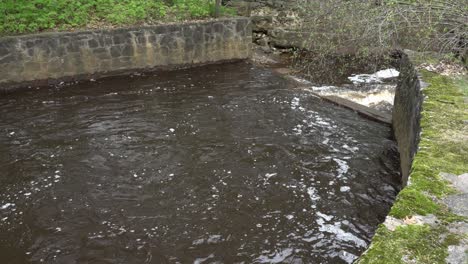 we see a beautiful view of a small river with stone walls on both sides. additionally, there is some greenery on top of the stones, which makes it truly lovely.