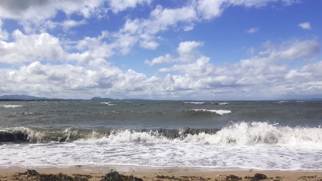 바람 부는 여름날 모래 위에 해초가 있는 모래사장에 부서지는 파도의 고정 샷 | 포토벨로 비치, 에딘버러 | 시네마틱 24fps로 hd로 촬영