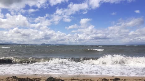 A fixed shot of waves breaking on a sandy beach with seaweed on the sand, on a windy summer day | Portobello beach, Edinburgh | Shot in HD at cinematic 24 fps