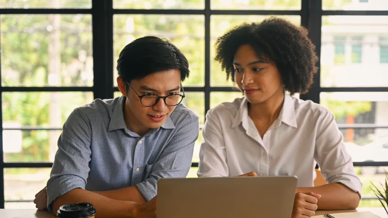 Vertical video: Giving thumbs-up, pair in shirts shifting into focused review over laptop by window