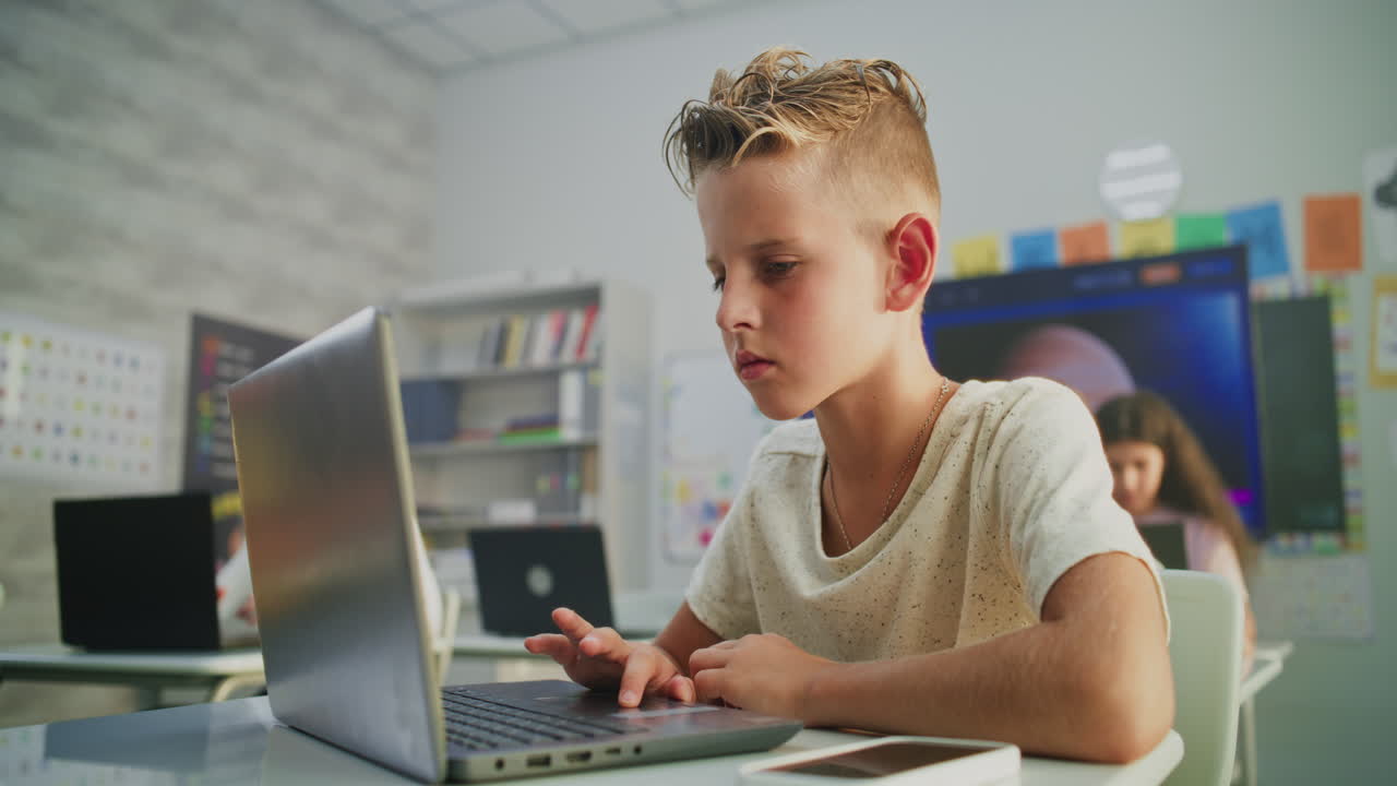 Smiling elementary school boy uses laptop computer in classroom