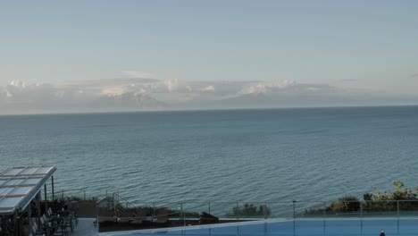 wide panning shot of a coast view from the beautiful swimming pool to deep-sea with some mountains in the background