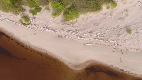 Aerial-top-down-view-of-people-walking-through-a-landscape-with-dunes-and-a-lagoon-at-sunset