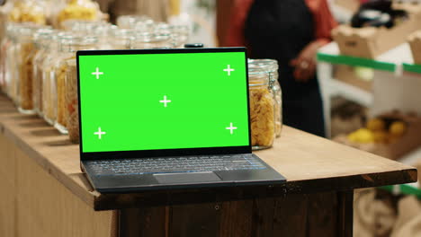 computadora que muestra una pantalla de chromakey en blanco junto a las mercancías en frascos