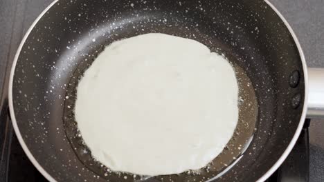 close-up shot wet pancake batter being poured into a metal pan with oil top view