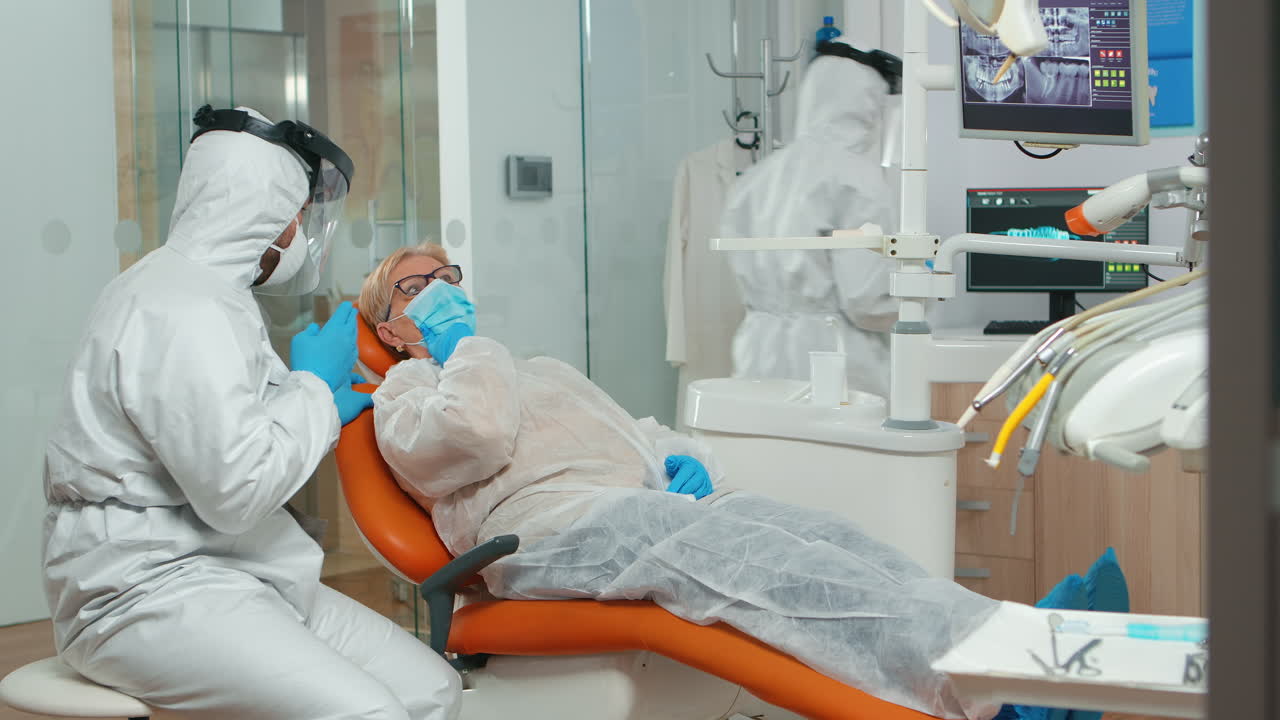 보호복 을 입은 치과 의사 가 치통 을 고 있는 환자 와 대화 하고 있다