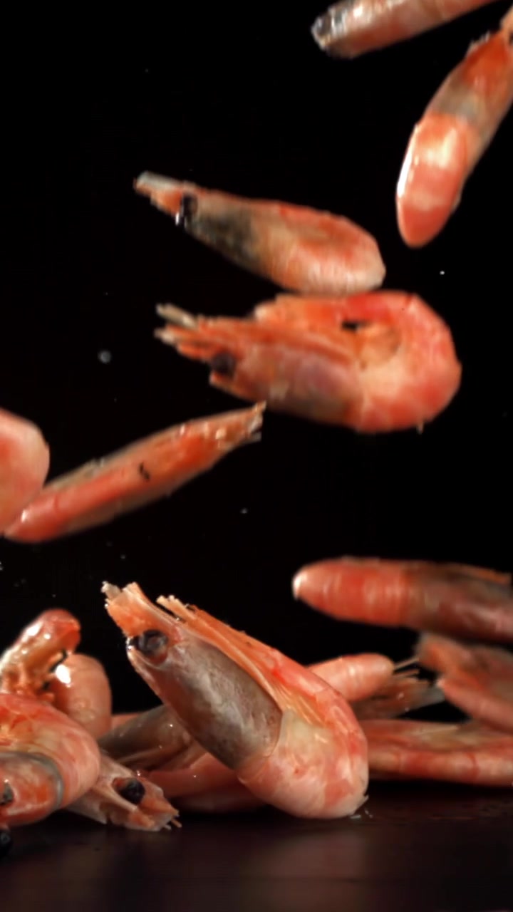 Camarones cocidos y granos de pimienta cayendo en cámara lenta sobre fondo negro