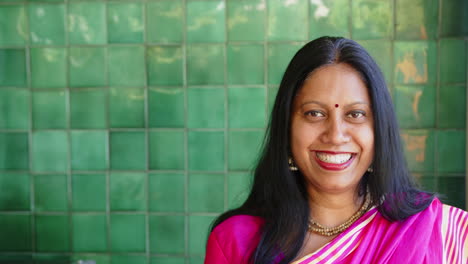 smiling indian woman in traditional indian sari standing against green tiled wall, copy space