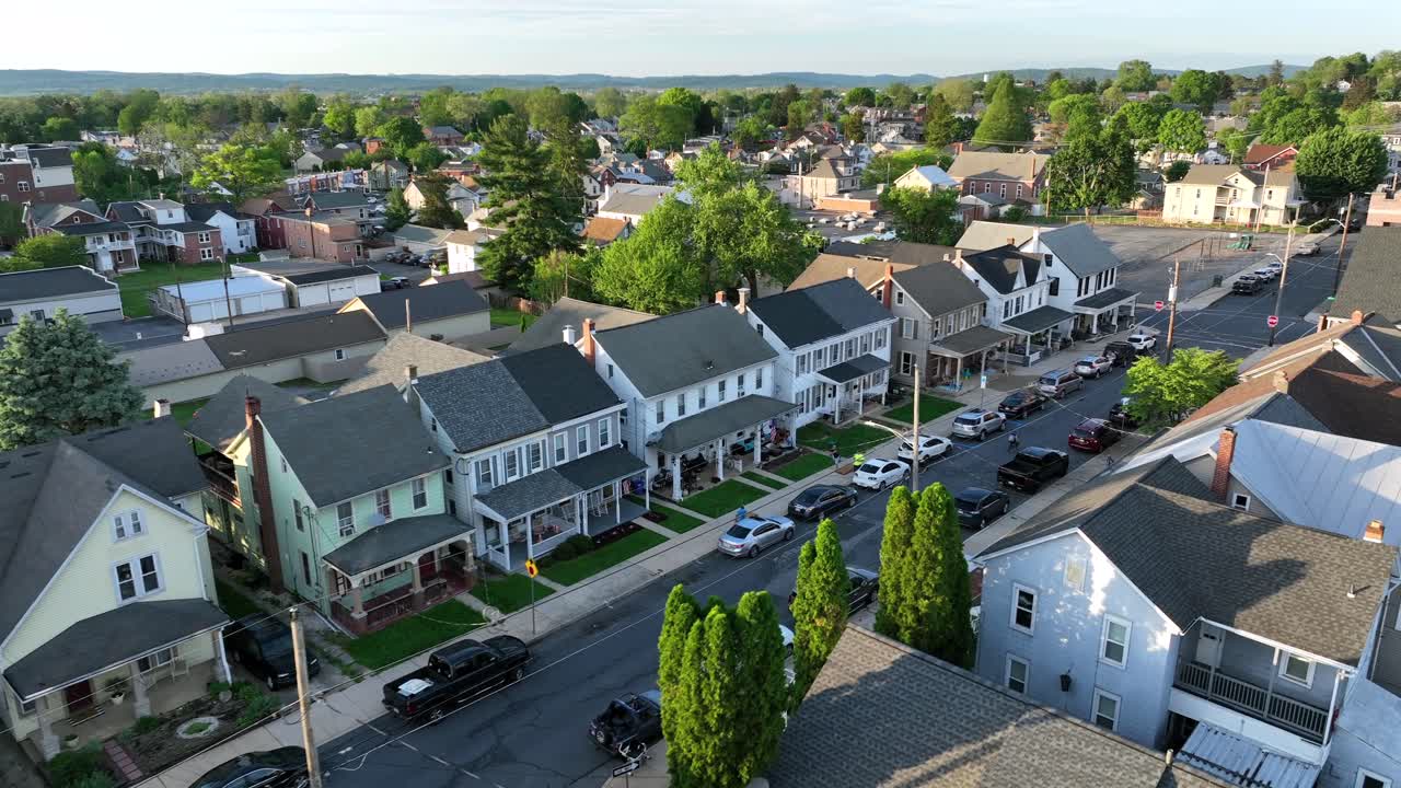 Row of houses with porch and front yard in american town at sunset. Ephrata City in Pennsylvania. Parking cars along road. Aerial approaching wide shot.
