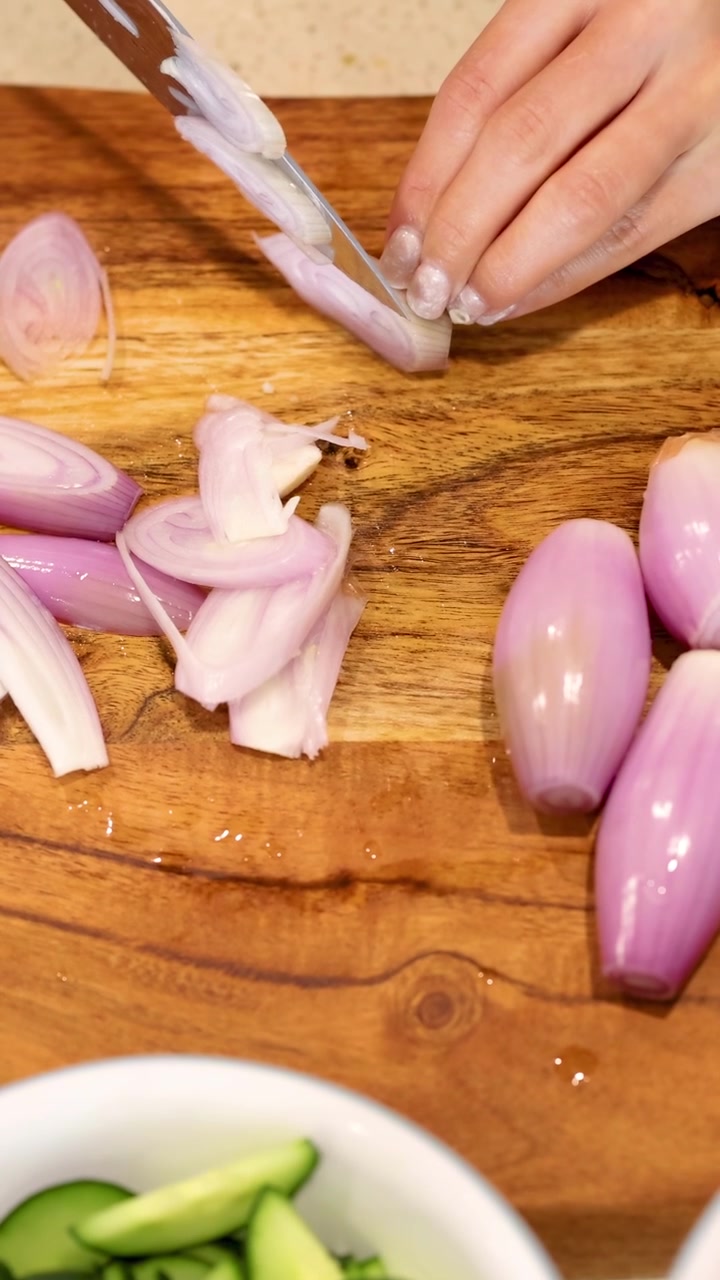 Una persona affetta scalogni su un tagliere di legno in una cucina ben illuminata, mostrando abilità precise con il coltello