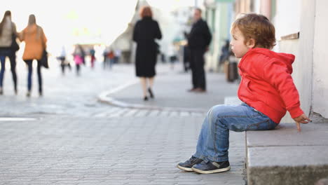 little boy sitting alone in the street people passing by