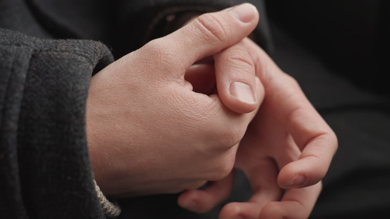 Primo piano delle mani irrequiete di un creatore caucasico, manica di lana visibile, pollice che sfrega l'unghia, nocche tese, movimento sottile durante una riflessione silenziosa, ruoli che cambiano da designer a scrittore a fotografo, stato d'animo