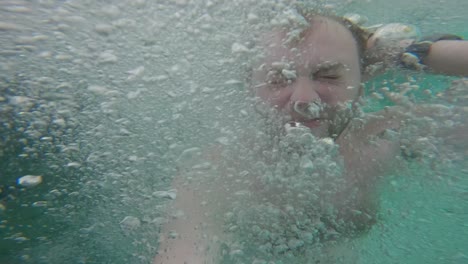 hombre sumergido bajo el agua, rodeado de burbujas, luego emergiendo en el kali biru dentro del bosque tropical en raja ampat, papúa occidental, indonesia