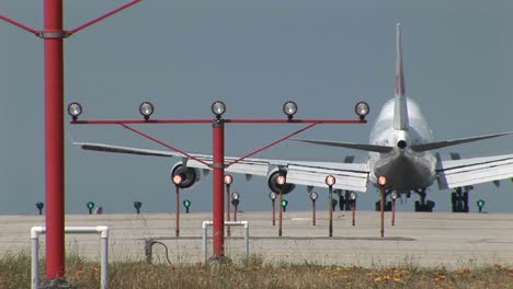 a 747 jet lands on an airport runway behind lights and guide beacons