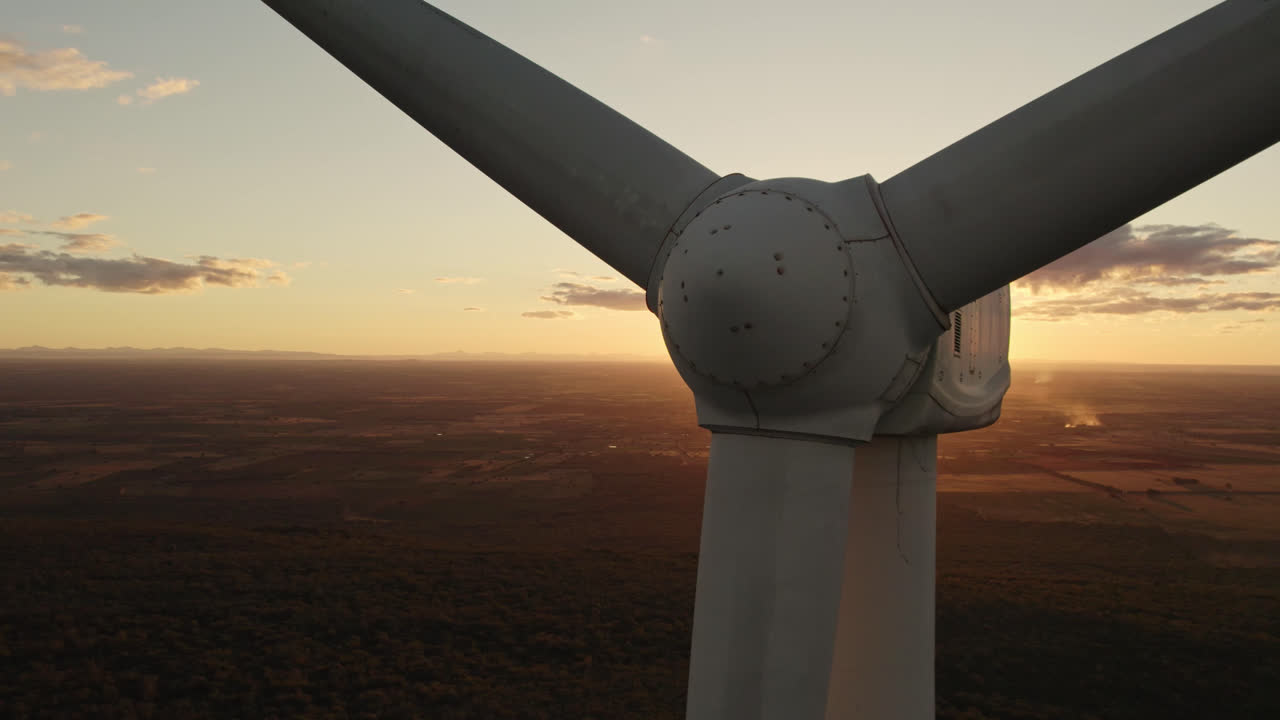 Aerial circling wind turbine occluding sunshine during beautiful orange sunset. Close up showing Nacelle