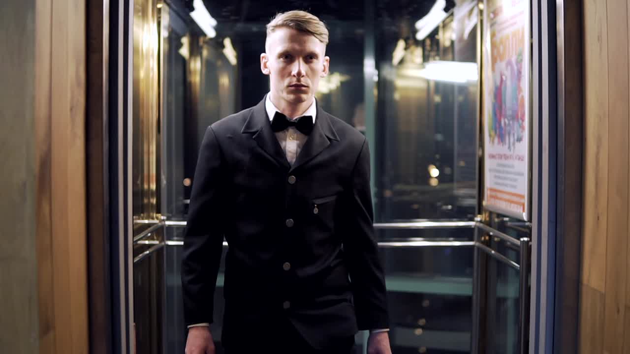 유리 문으로 엘리베이터에서 나오는  ⁇ 타이를 입은 젊고 성공적인 사업가